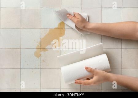 Frau wischt verschütteten Kaffee mit Papierservietten auf weißem Fliesenhintergrund ab Stockfoto