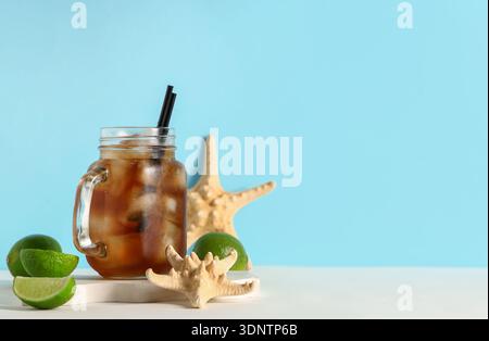 Mauerglas mit kaltem Cuba Libre Cocktail mit Sternenfischen und Gipspodium auf weißem Tisch vor blauem Hintergrund Stockfoto