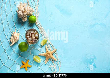 Glas kalter Cuba Libre Cocktail mit Sternenfischen, Muscheln und Korallen auf blauem Hintergrund Stockfoto