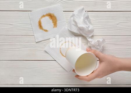 Weibliche Hand mit Papierbecher, Servietten und Kaffeeflecken auf weißem hölzernem Hintergrund Stockfoto