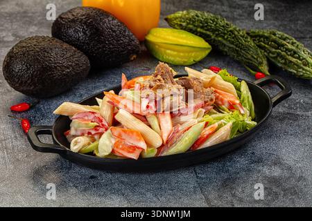 Appetitlicher Nudelsalat mit Thunfisch und Gemüse in einer cremigen Sauce. Die Top-Down-Ansicht auf dunklem Hintergrund hebt frische rote, grüne und beige Farben hervor. P Stockfoto