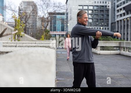 Senior Mann und Frau, die sich in Sportbekleidung auf der plaza ausstrecken und gehen, von Betontopf, Kopierraum Stockfoto
