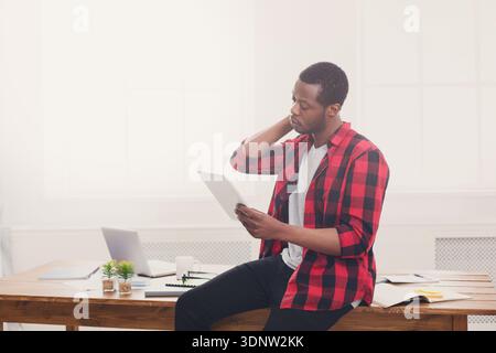 Gestresster schwarzer Geschäftsmann im modernen Büro, mit Tablet arbeiten Stockfoto