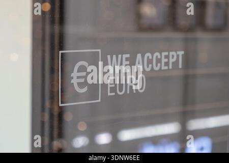Aus nächster Nähe des Euro-Währungssymbols AKZEPTIEREN WIR EURO-Text auf einem Glaseingang, der die finanzielle Inklusivität für verschiedene Kunden und gl hervorhebt Stockfoto