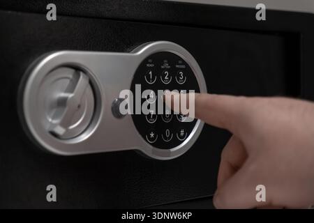 Nahaufnahme einer Hand, die Zahlen auf einem eleganten schwarzen elektronischen Safe mit silberner Tastatur drückt, die sichere Aufbewahrung wichtiger Dokumente und Dokumente darstellt Stockfoto