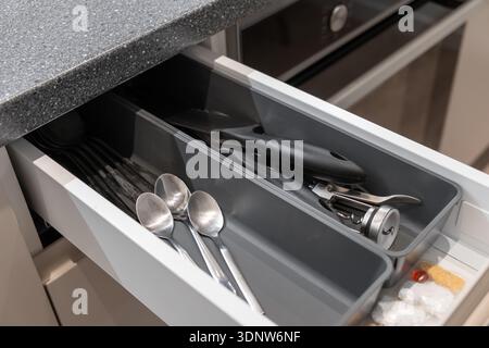 Nahaufnahme einer modernen Küchenschublade mit grauem Organizer mit glänzenden Löffeln, wichtigen Kochutensilien und kleinen Gegenständen Stockfoto