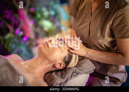 Verträumte Frau erhält heilende entspannende Gesichtsmassage mit Aromaölen in der Schönheitsklinik Stockfoto