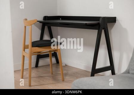 Blick auf einen einfachen schwarzen Schreibtisch mit hellem Holzstuhl, perfekt für ein modernes Heimbüro oder Arbeitszimmer, minimalistisches Dekor und effiziente Arbeitszimmer Stockfoto
