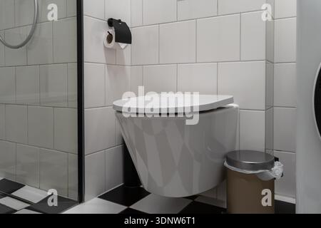 Sauberes, modernes Badezimmer mit Toilette, schwarzem Toilettenpapierspender und kariertem Boden, das einen modernen, persönlichen Touch bietet Stockfoto