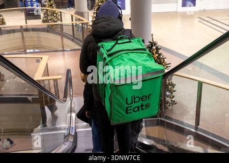 Krakau, Polen - 30. November 2025: Uber isst einen Beutelträger auf einer Rolltreppe im Einkaufszentrum und zeigt moderne urbane Essenslieferungen, Komfort und festliche Feiertage Stockfoto
