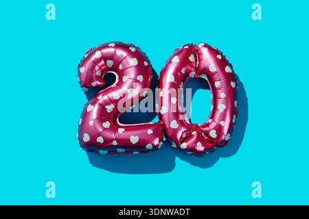 Zwei Folienballons mit rosafarbenem Herzmuster, die die Zahl 20 bilden, ruhen auf einem hellblauen Hintergrund, wobei starkes Licht klare Schatten erzeugt, die t verstärken Stockfoto