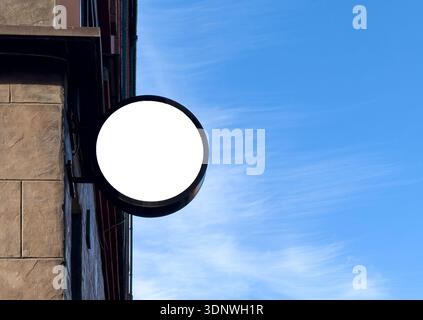 Leeres, rundes Ladenschild, das an einer Ziegelfassade vor blauem Himmel angebracht ist. Minimales Modell für den Außenbereich bietet leeren Kreis geeignete Branding-Logos Werbung. Stockfoto