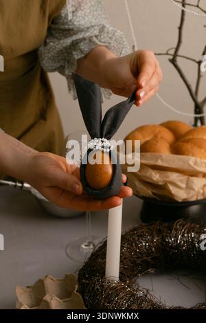 Lächelnd bereitet die Frau den Ostertisch vor, bemalt Eier und arrangiert Kerzen und Geschirr für eine Familienfeier. Stockfoto