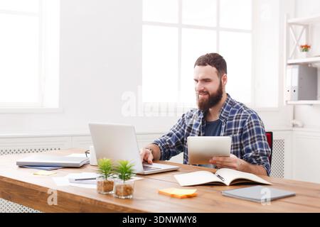 Junger, lächelnder Mann, der in einem modernen weißen Büro einen Laptop benutzt Stockfoto