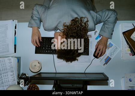 Junge Frau, die während der Arbeit im Büro Kopf auf dem Schreibtisch ruht Stockfoto