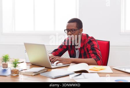 Junger schwarzer Geschäftsmann, der mit Laptop arbeitet Stockfoto