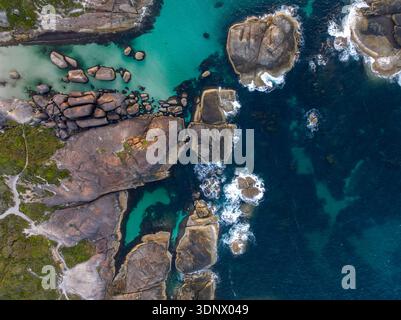 Luftbild von oben nach unten von großen Granitblöcken, türkisfarbenen Küstenbecken und dunklen Meeresriffmustern in der Nähe einer zerklüfteten Küste in Western Australia. Stockfoto