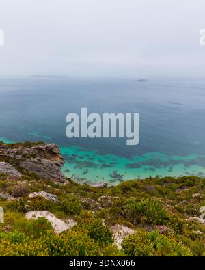 Ein hoher Aussichtspunkt an der Küste mit Blick auf türkisfarbene Untiefen, tiefes Ozeanwasser und zerklüftete Vegetation. Stockfoto