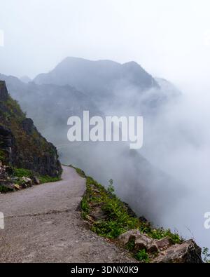 Eine schmale Bergstraße schlängelt sich entlang steiler Klippen, während dichter Nebel über den Ma Pi Leng Pass in Nordvietnam driftet. Stockfoto