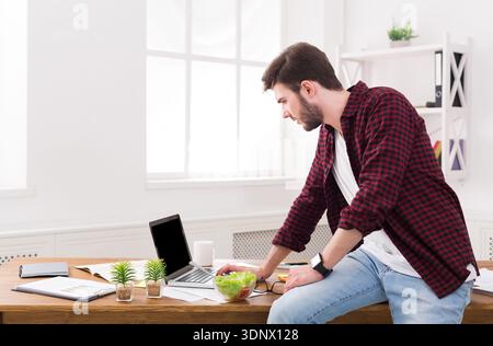 Junger seriöser Geschäftsmann mit Laptop im Büro Stockfoto