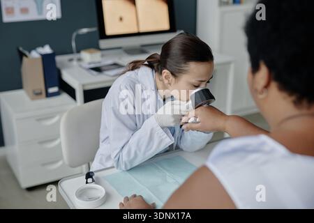 Junge asiatische Dermatologin untersucht die Hand einer Schwarzen Frau mittleren Alters Stockfoto