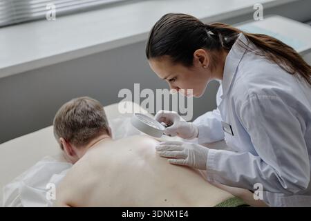 Kaukasische Dermatologin untersucht Rücken eines kaukasischen Mannes mittleren Alters Stockfoto
