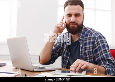 Nahaufnahme eines seriösen männlichen IT-Managers liest einen Bericht, während er mit offenem Netbook am Tisch sitzt. Stockfoto