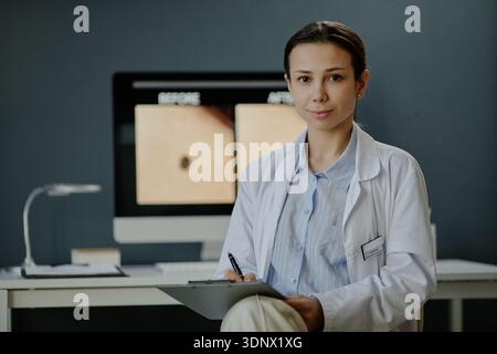 Lächelnde junge kaukasische Dermatologin, die Clipboard im Büro hält Stockfoto