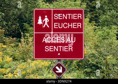Rotes Informationsschild mit der Aufschrift „Sentier Eucher Trail“ (Eucher Trail) und „Acces au sentier“ (Zugang zum Weg), das den Eingang zum Eucher Trail in der Nähe von La Baie kennzeichnet Stockfoto