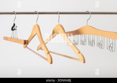 Leere verschiedene hölzerne Kleiderbügel Gruppennahmeband auf Metallschiene vor weißem Wandhintergrund. Zubehör für Haushalt und Geschäft. Stockfoto