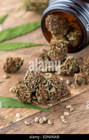 Getrocknete weibliche Knospen von Marihuana-Blüten mit Hanfblättern. Cannabis-Unkrautknospen liegen im Glasgefäß und auf einem Holztisch. Hanfknospen-Nahaufnahme. Freizeit märz Stockfoto