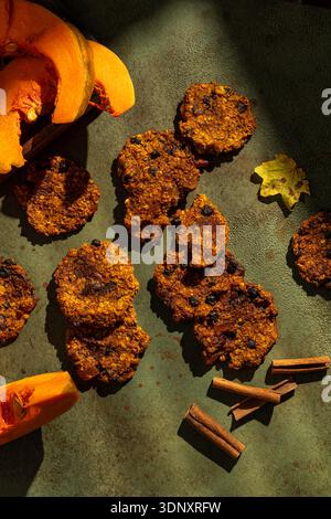Köstliche vegane Kürbiskekse mit Rosinen auf einer strukturierten Oberfläche, begleitet von Kürbisscheiben und Zimtstäbchen, schaffen eine warme Atmosphäre für ein heiteres Klima Stockfoto