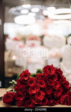 Ein wunderschöner Blumenstrauß aus leuchtenden roten Rosen, elegant angeordnet und auf einer Holztheke in einem Blumengeschäft ausgestellt. Perfekt für romantische Anlässe oder als Stockfoto