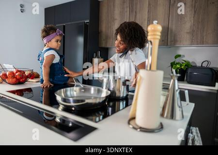 Mutter und Tochter genießen eine gute gemeinsame Zeit in einer modernen Küche, in der Familienbande und Alltagsmomente hervorgehoben werden. Das Zimmer ist stilvoll und modern Stockfoto