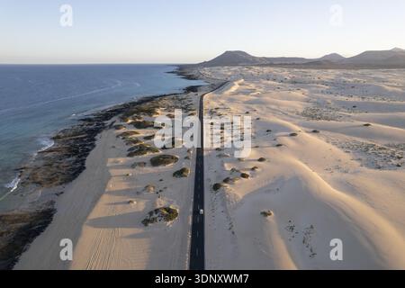 Aus der Vogelperspektive auf den starken Kontrast zwischen dem türkisfarbenen Meer und den goldenen Sanddünen entlang der Küste, Corralejo, Kanarischen Inseln, Spanien. Stockfoto