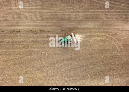 Luftaufnahme eines grünen Traktors, der auf einem großen Pflugfeld arbeitet. Die Maschine bewegt sich über das braune Gelände und hinterlässt eine Spur von Staub, während sie sich vorbereitet Stockfoto