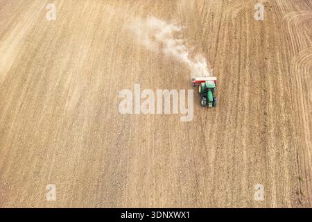Aus der Vogelperspektive eines Traktors, der ein weites Feld pflügt und ordentliche Bodenreihen hinterlässt. Die Maschine verteilt Staub, während er sich über das weitläufige Ackerland bewegt. Stockfoto