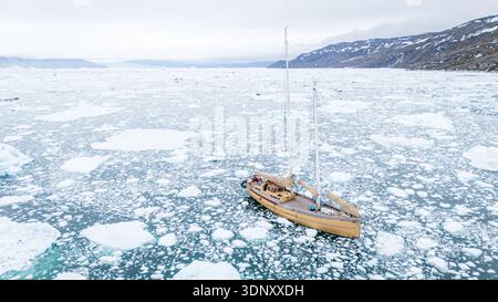 Ein einsames Segelboot navigiert durch die eisigen Gewässer der Davis-Straße in Grönland, umgeben von schwimmenden Eisbergen. Die beschauliche Szene fängt die krasse Schönheit ein Stockfoto