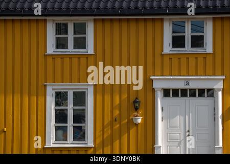 Nahaufnahme einer hellgelben Holzfassade auf den Lofoten-Inseln, Norwegen, mit weißen gerahmten Fenstern und einer Tür, die nordische Architektur einfängt Stockfoto