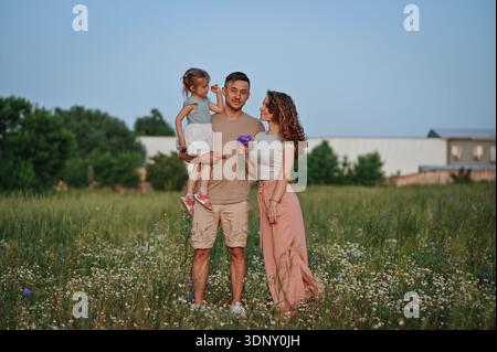 Eine Familie genießt einen ruhigen Spaziergang in einem üppigen grünen Feld, umgeben von Wildblumen. Sie teilen ein Lächeln unter dem blauen Himmel und genießen die Schönheit und Schönheit der Natur Stockfoto