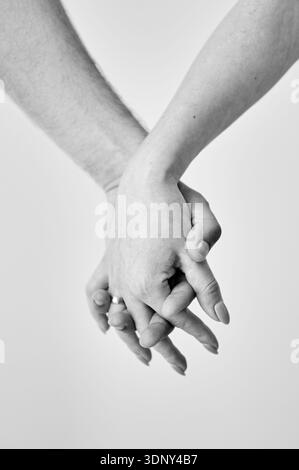 Zwei Hände in der Hand vor neutralem Hintergrund gehalten. Nahaufnahme der Hand von Mann und Frau. Konzept von Intimität, Unterstützung und Vertrauen. Schwarzweißbild. Stockfoto