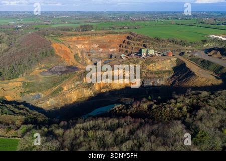 Aus der Vogelperspektive auf eine dramatische Steinbruchlandschaft, in der Erdtöne auf dichtes Grün treffen, kontrastierende Texturen unter einem riesigen Himmel, La Roche-Jaudy, Bretagne, Fr. Stockfoto