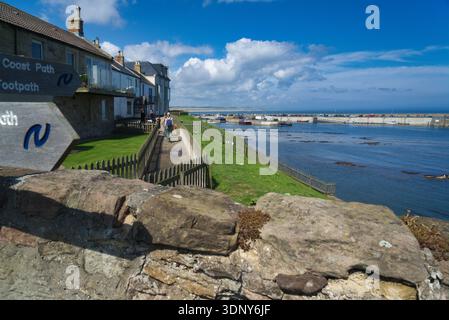 Seahouses Harbour. Blauer Himmel und Sonnenschein. Küstenpfad Wegweiser Walkers. Seahouses ist ein beliebtes Fischerdorf am Meer in Northumberland. UK Stockfoto