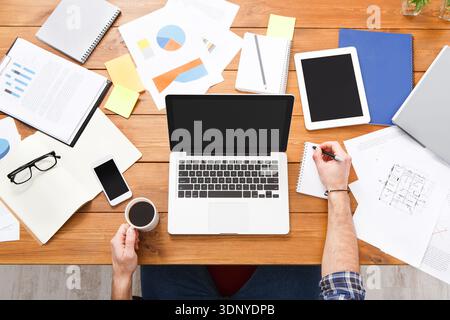 Geschäftsmann von oben mit Laptop und Analyse von Investitionstabellen auf dem Schreibtisch. Stockfoto