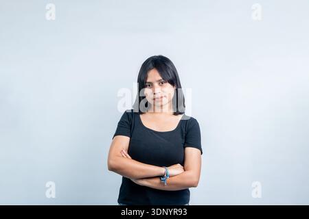 Porträt einer jungen südostasiatischen Frau in einem schwarzen Hemd mit überkreuzten Armen. Selbstbewusste Studioaufnahmen auf hellgrauem Hintergrund. Stockfoto