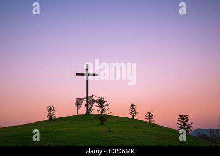 Das Kreuz ist auf einem grasbewachsenen Hügel und einer Wiese in der Dämmerung, abstrakter Natur als Christentum-Konzept begraben. Stockfoto