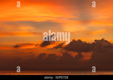 Ruhiger Sonnenuntergang im Ozean mit orangefarbenem Himmel und verstreuten Wolken Stockfoto
