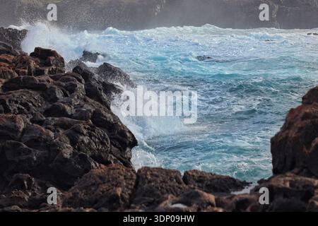 Hohe Wellen aus dem türkisfarbenen Wasser des Atlantischen Ozeans treffen auf die schwarzen Felsen am Strand Stockfoto