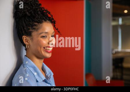 Afroamerikanerin lehnt sich an die weiße Wand, lächelt, trägt blaues Polka-Shirt, Kopierraum Stockfoto