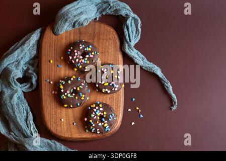 Eine rustikale Schoko-Donuts mit fröhlichen Streuseln, elegant auf einem hölzernen Schneidebrett angeordnet, präsentiert ein warmes und einladendes Ambiente Stockfoto